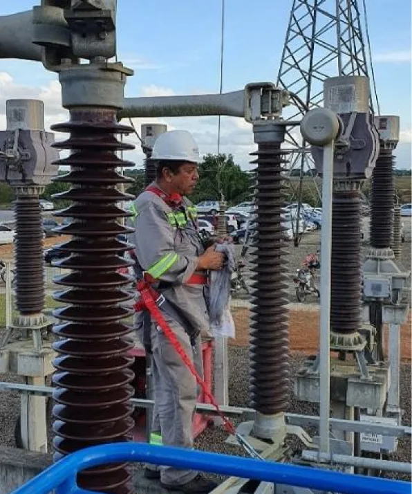 Técnico de capacete trabalhando entre os isoladores de uma subestação a céu aberto