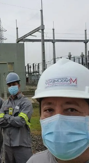 Engenheiro de capacete com a marca MNascimento e máscara diante de uma subestação